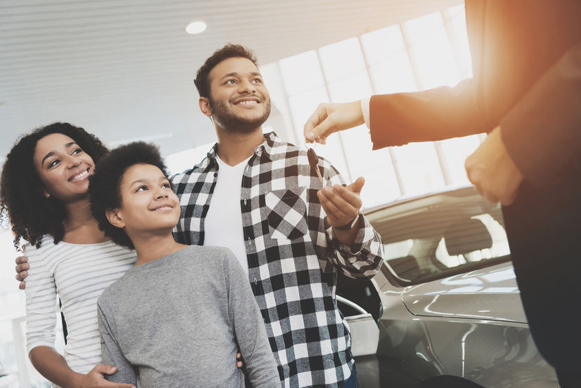 African american family at car dealership. Salesman is giving keys for new grey car. Be one solutions