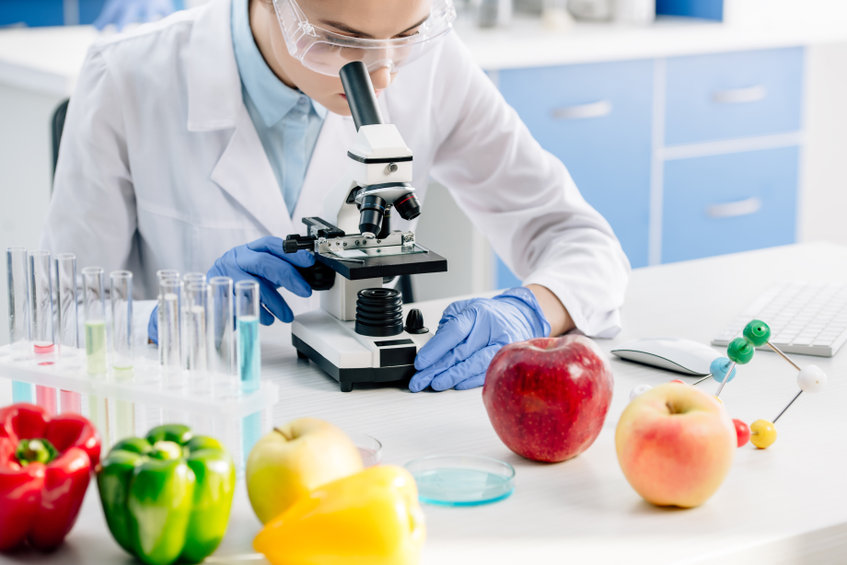 view of a molecular nutritionist using a microscope and sitting at the table surrounded by fruits and vegetables